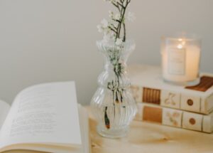 A serene composition featuring a vase with white blossoms, books, and a lit candle.