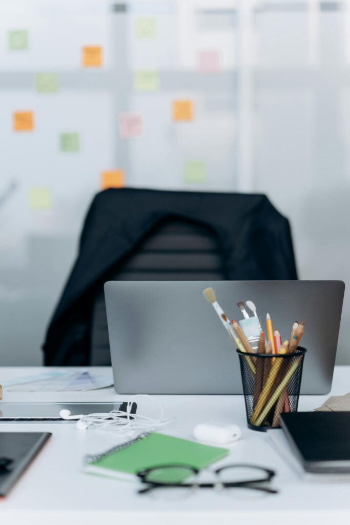 Stylish office desk with a laptop, stationery, and notes on glass wall.